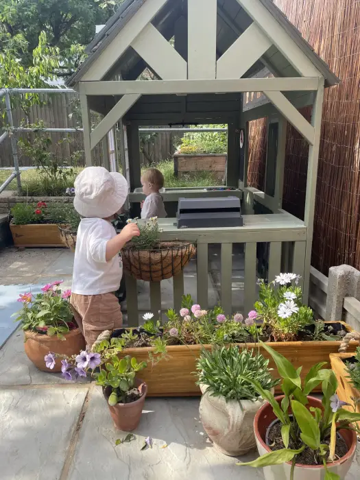 Two children planting flowers by the garden playhouse