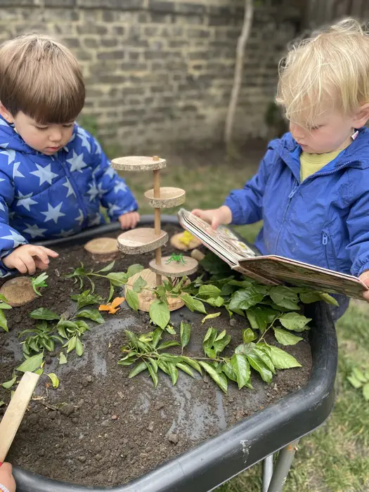 Two children exploring leaves and wood slices in a nature tray