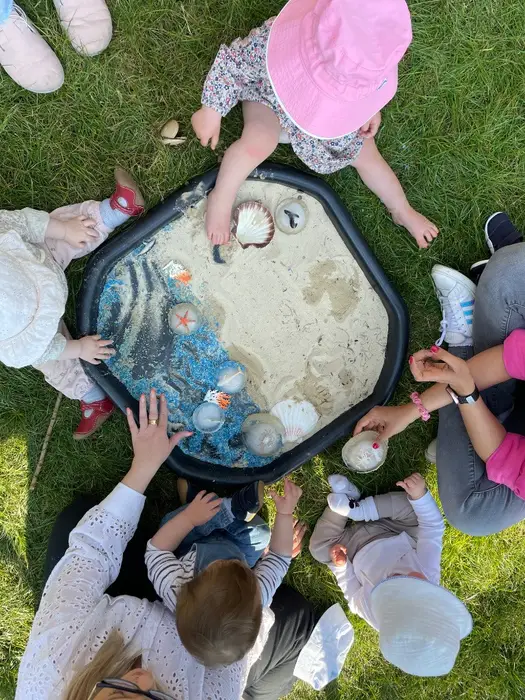 Children playing together around a sand tray on the grass